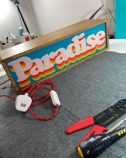 Illuminated light box, cyan and orange, retro 'Paradise' layered typography in wooden frame